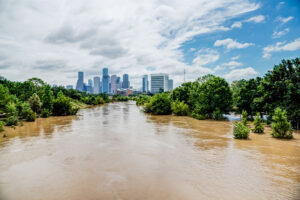 High and fast water rising in Bayou River with downtown Houston in background under cloud blue sky. Heavy rains from Harvey Tropical Hurricane storm caused many flooded areas in greater Houston area.