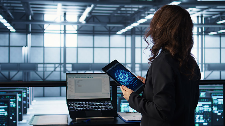 Technician in data center with tablet integrating AI driven automation tools, running predictive maintenance routines. Woman ensuring continuous uptime of server room and managing data flows